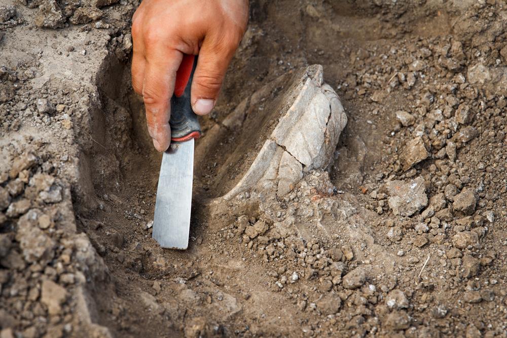 A hand digging up an ancient clay artifact