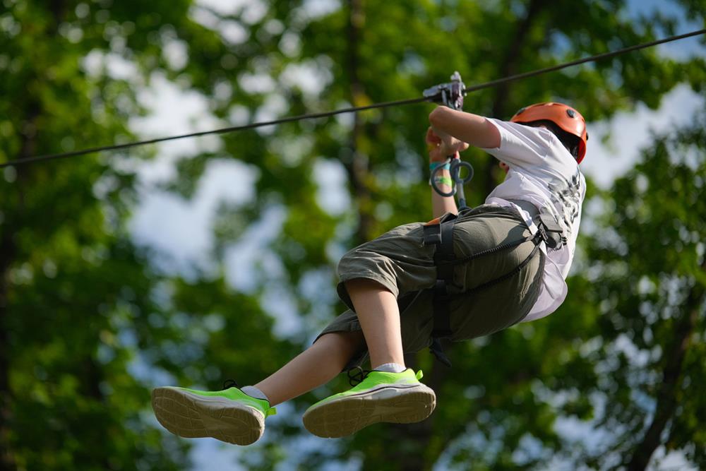 Teenage boy on zipline having fun at outdoor extreme adventure park