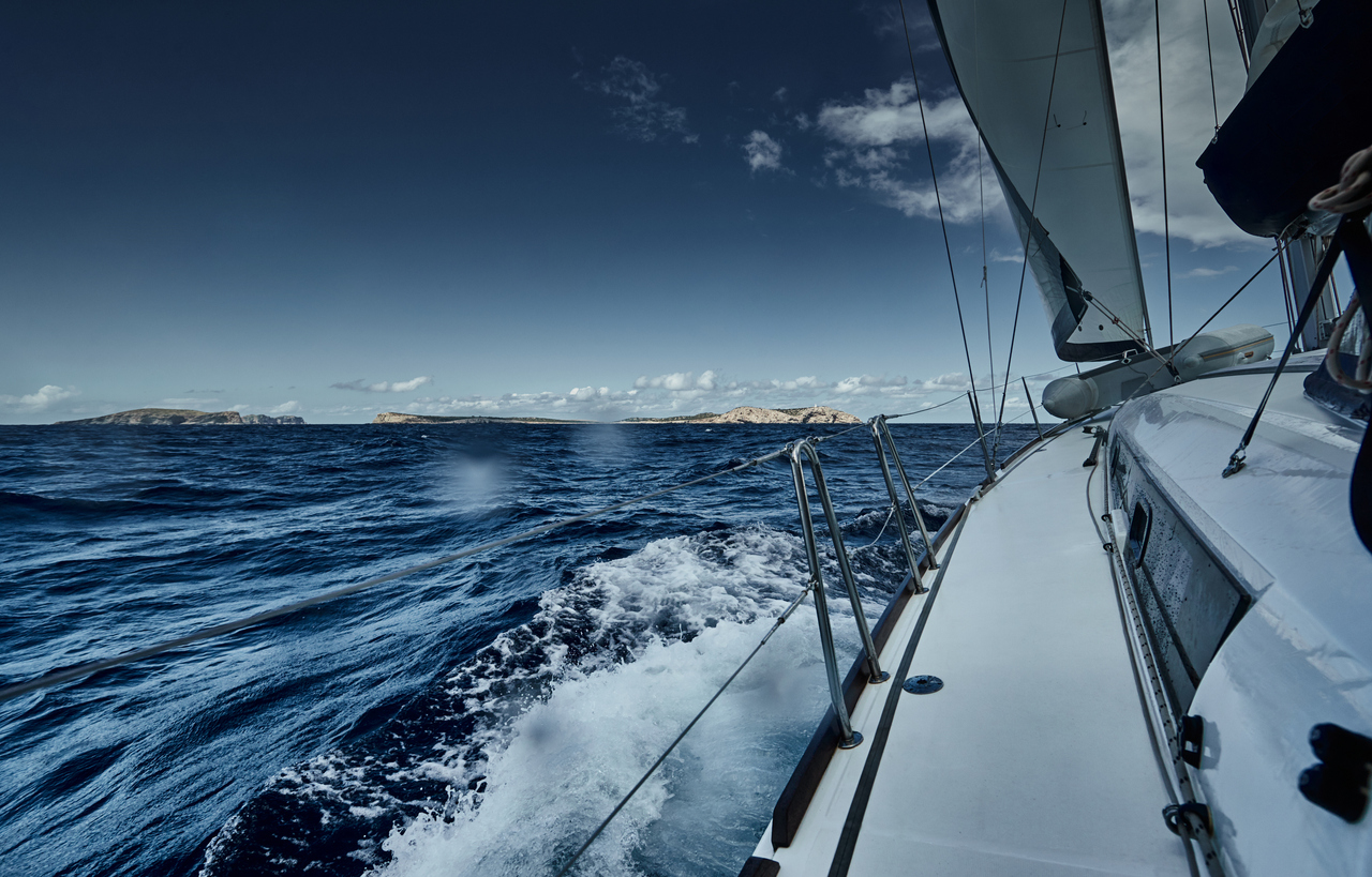 The view of the sea and mountains from the sailboat, edge of a board of the boat, slings and ropes, splashes from under the boat, sunny weather, dramatic sky