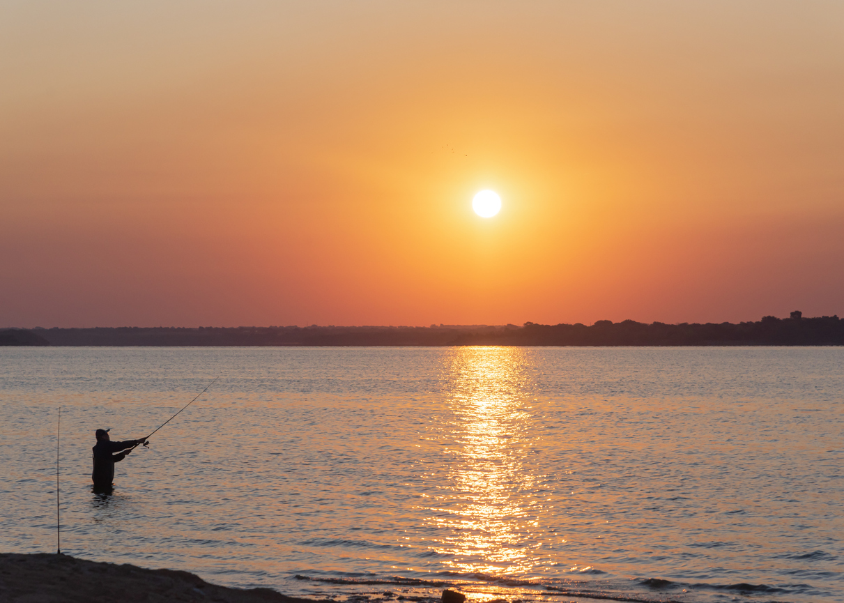 Wade fishing at sunrise with Asian man fishing spin casting at Lavon Lake near Dallas