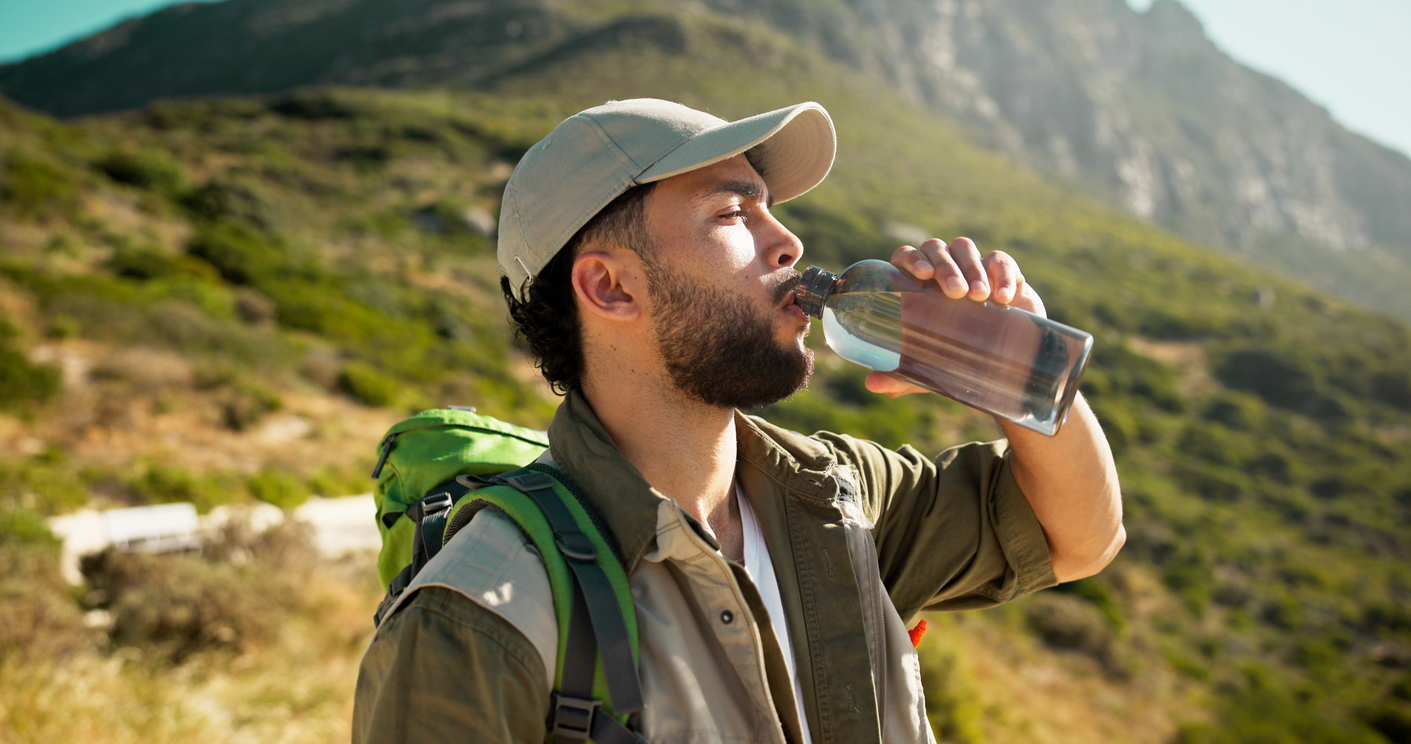 Mountain, drinking water and man with break for hiking, hydration or summer tourism for travel trip. Outdoor, wellness and person relax with liquid bottle, trekking or thirsty on sightseeing vacation