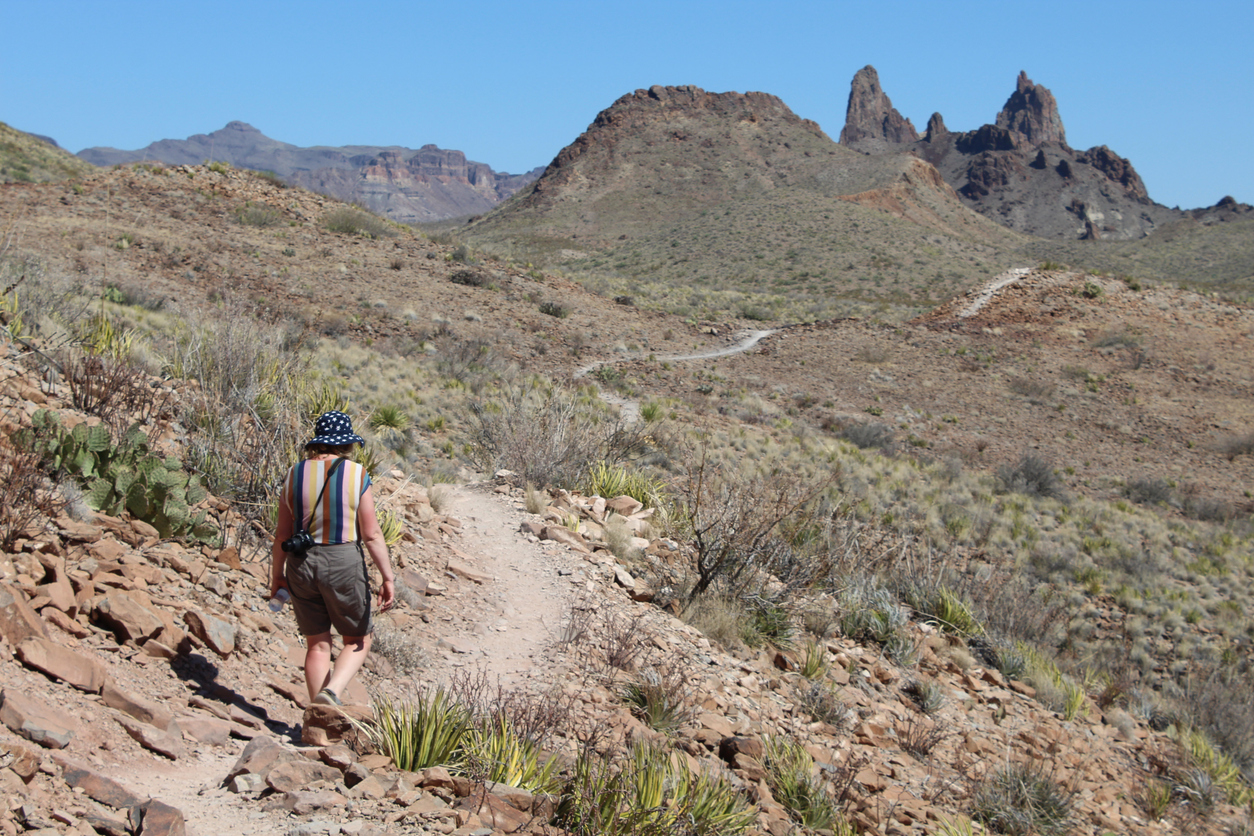 Woman with a camera walking on a narrow trail towards a mountain at Big Bend National Park in Texas