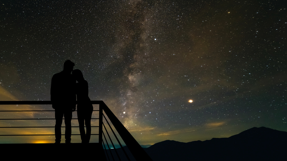 The romantic couple standing on the balcony on the scenic starry sky background